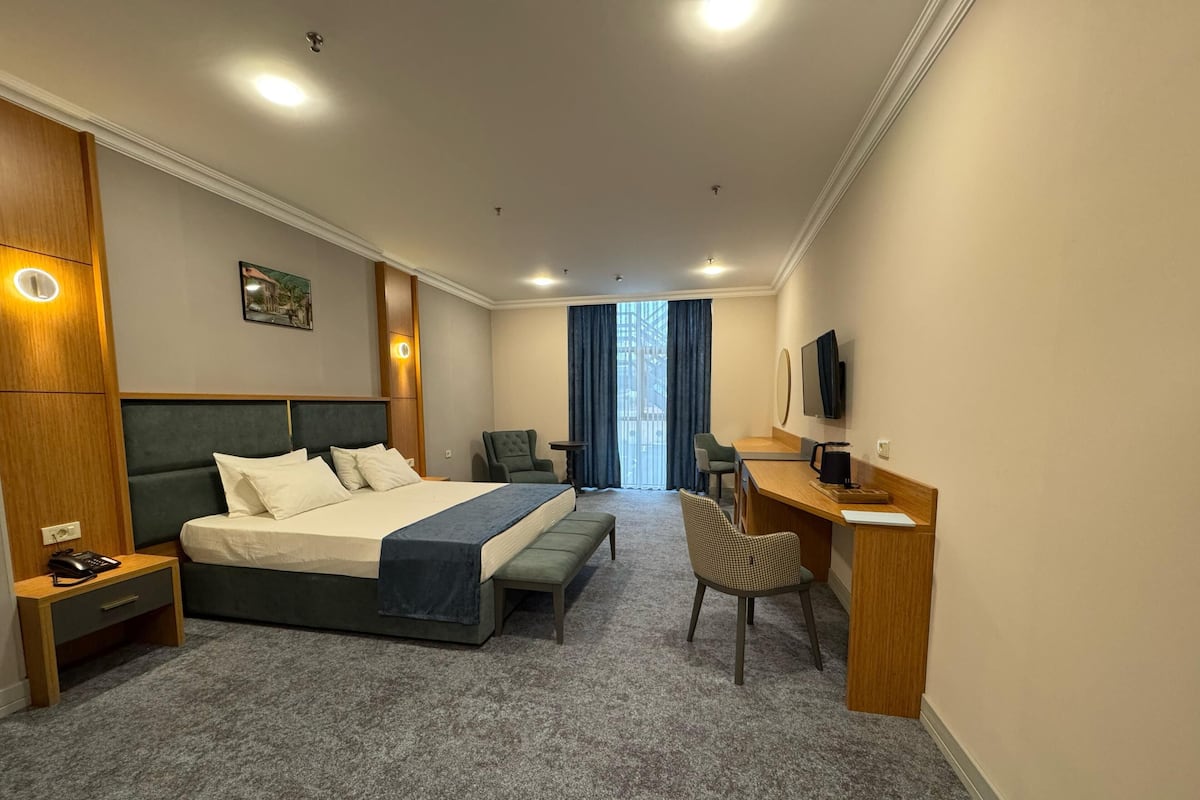 A hotel room with a large bed, a desk with a chair, a TV, and a window with curtains.