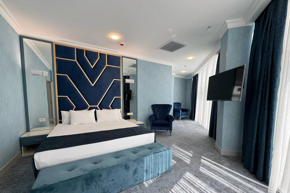A modern hotel room with a large bed, a seating area, a TV, and a mirror.