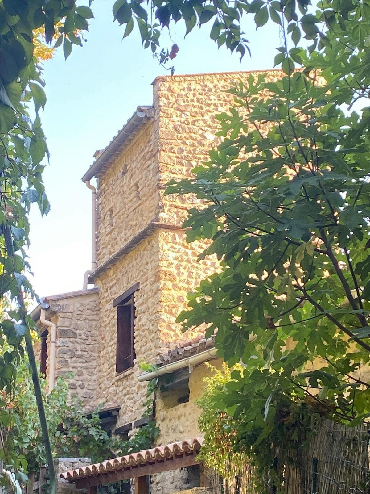 A stone building with a rustic facade, featuring a small balcony and a window with a shutter.
