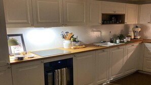 A kitchen with white cabinets, a wooden countertop, a built-in oven, and a coffee maker. - La Maison Madeleine (Nyons)