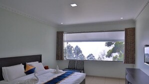 A modern hotel room with a large bed, a flat-screen TV, and a view of trees through the window. - Winter Garden Resorts (Munnar)