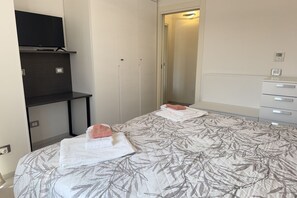 A hotel room with a bed, a TV on a shelf, a wardrobe, and a mirror. - In the Historic Centre, with a View of the Towers (Alba)