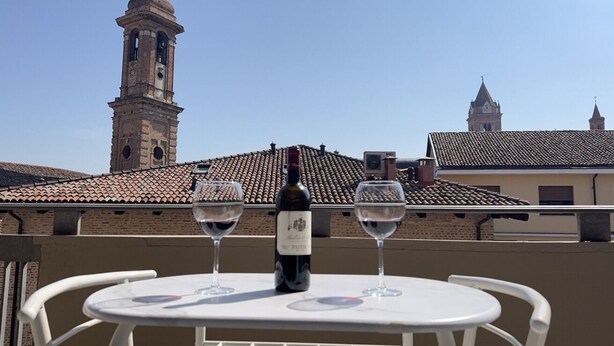 A balcony with a table, two wine glasses, and a bottle of wine. - In the Historic Centre, with a View of the Towers (Alba)