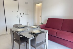 A dining area with a table set for four, a red sofa, and a door with a light switch. - In the Historic Centre, with a View of the Towers (Alba)