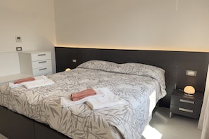 A neatly made bed with a leaf-patterned bedspread, a bedside table with a lamp, and a small drawer unit to the left. - In the Historic Centre, with a View of the Towers (Alba)