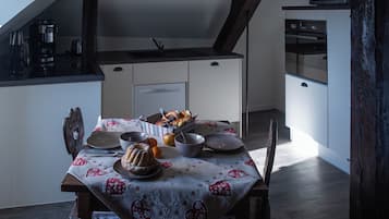 Una mesa de comedor servida con pan, frutas y un pastel, en una cocina con diseño moderno y vigas de madera.