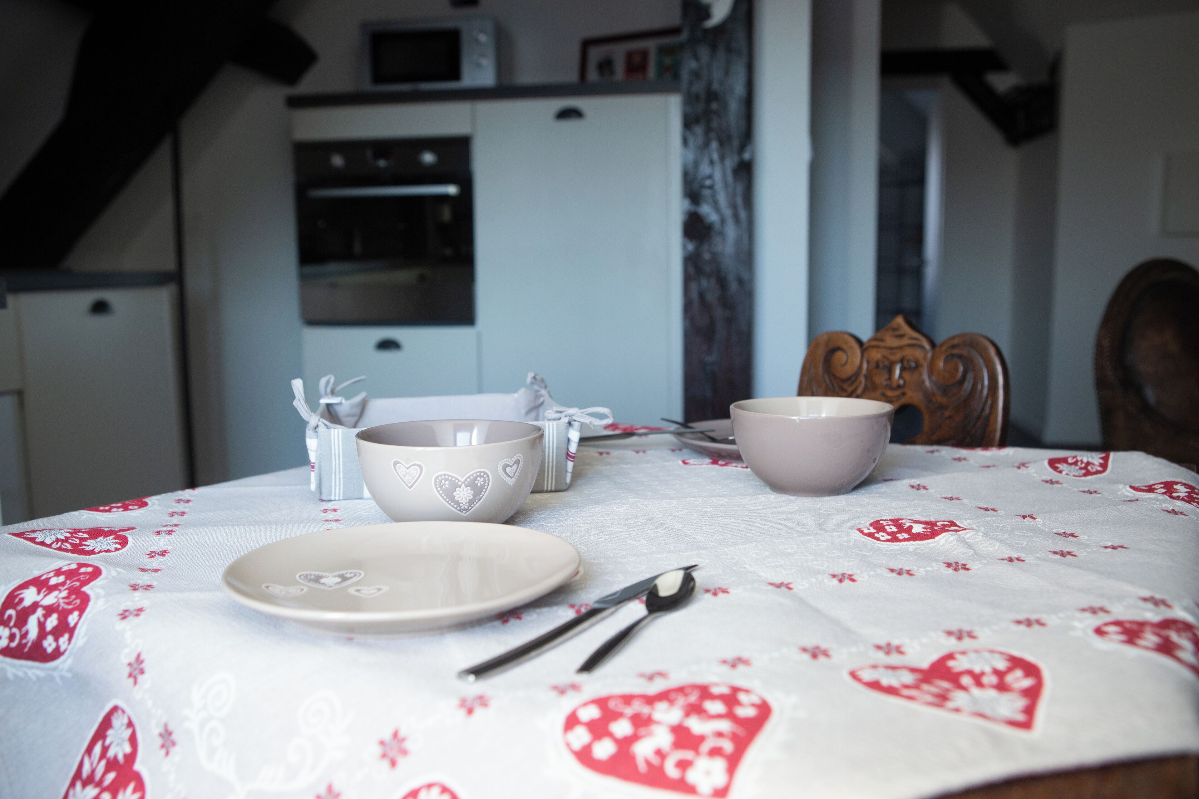 A dining table set with white plates, bowls, and cutlery, covered by a tablecloth with red floral patterns.