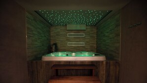 Een wellnessruimte met een groot bad, houten banken en een plafond met groene verlichting.