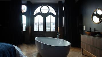 Un baño moderno con una bañera independiente, suelo de madera y vistas a la ciudad a través de amplias ventanas.