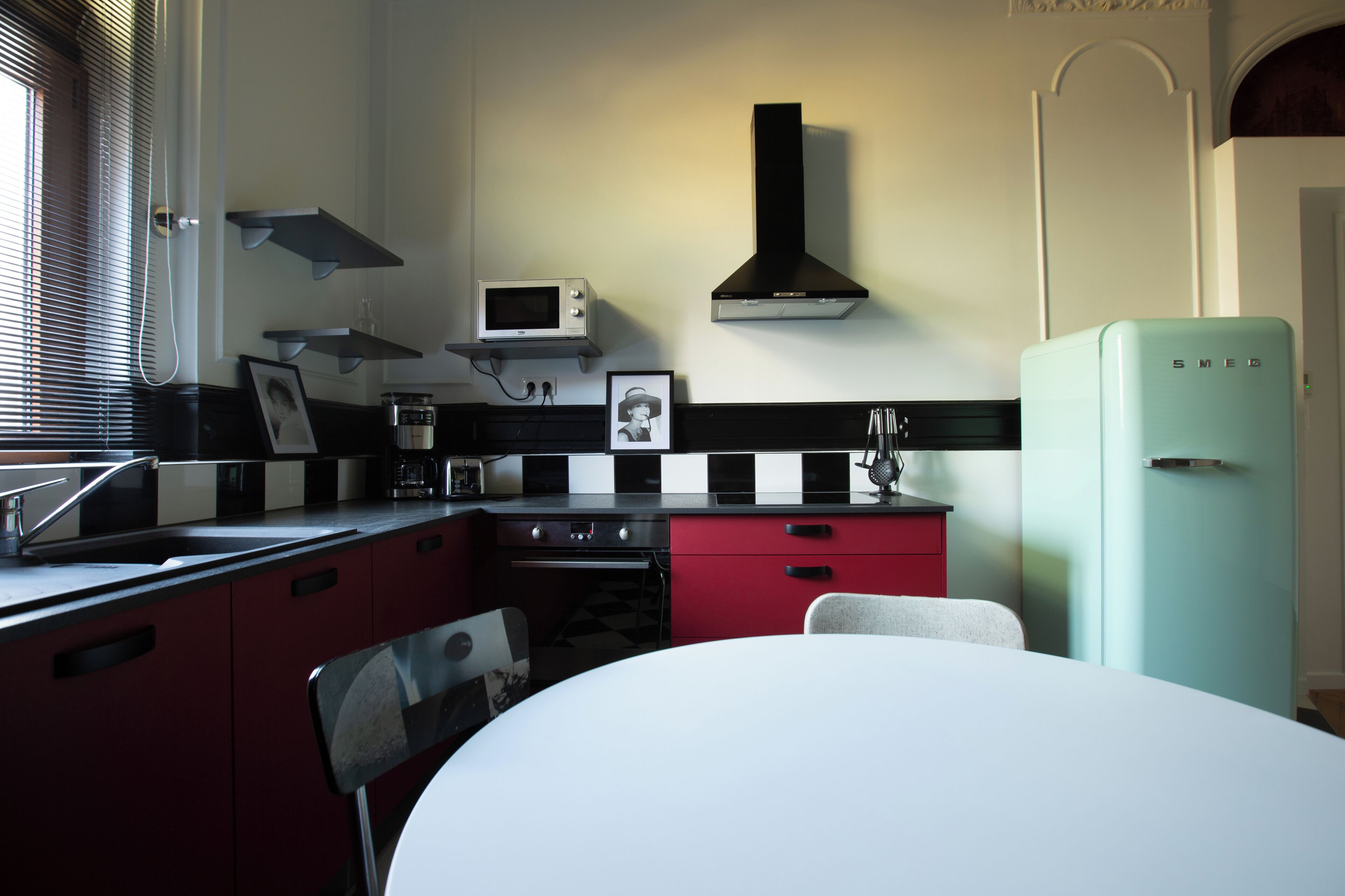 Cocina compacta con microondas, estufa y refrigerador. Hay una mesa de comedor con sillas y una ventana con persianas.