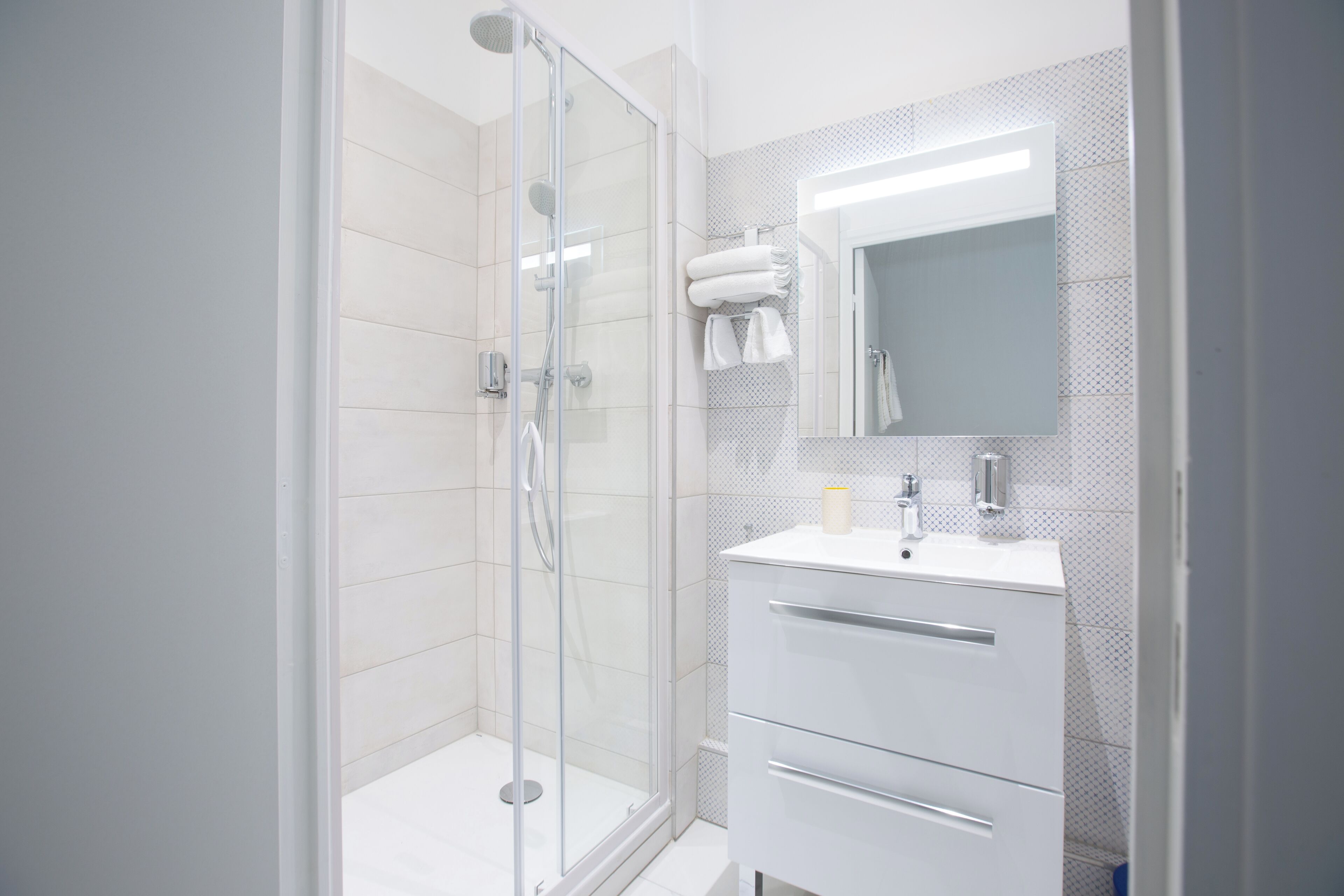 Une salle de bain moderne avec une douche à parois de verre, un lavabo blanc avec un miroir et un mur recouvert de carreaux.
