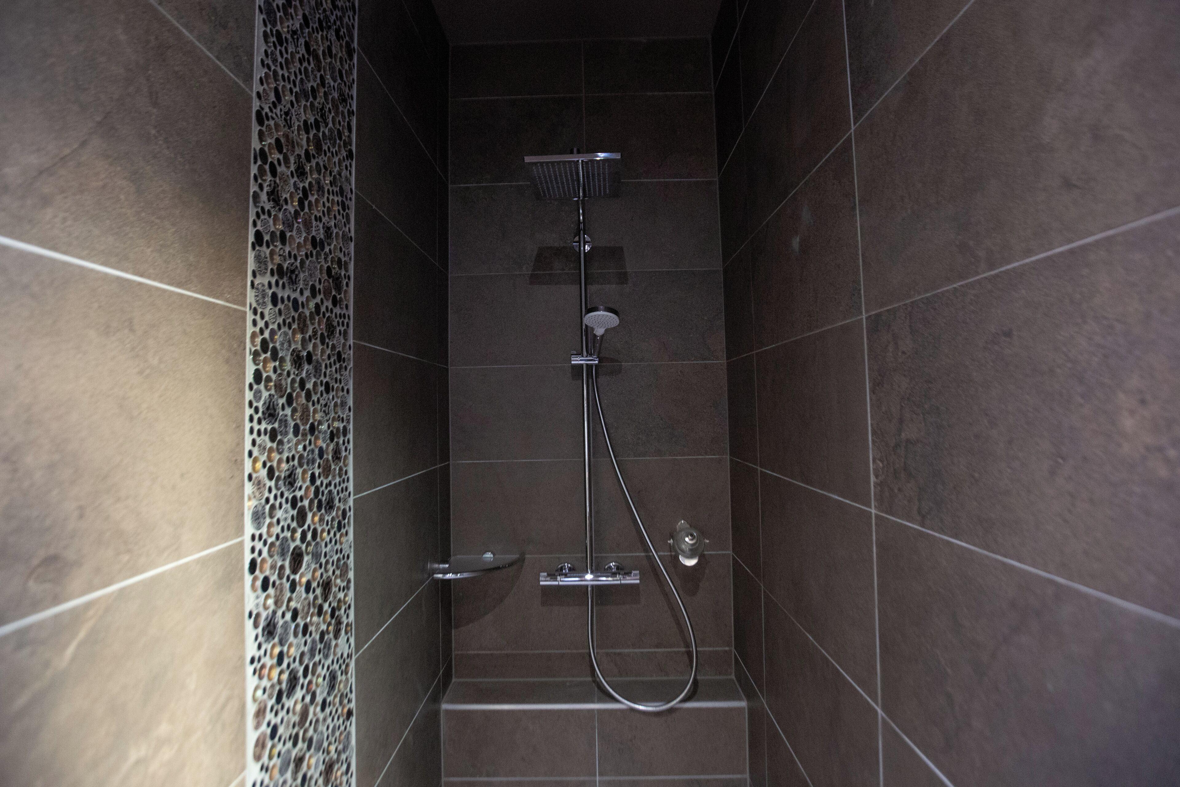 A modern shower with a handheld showerhead, a wall-mounted faucet, and a control panel.