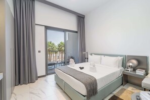 Une chambre d’hôtel moderne avec un grand lit, une table de chevet, une petite table et une vue sur les palmiers depuis le balcon.