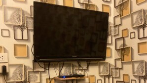 Une pièce avec un téléviseur fixé au mur, une chaise en bois et un papier peint à motifs.