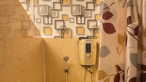 Un espace douche équipé d’un pommeau de douche à main, d’un panneau de commande fixé au mur et d’un distributeur de savon placé sur une étagère.