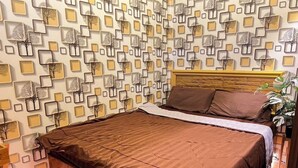 Une chambre à coucher avec un lit, une tête de lit, un mur orné d’un motif géométrique et une plante en pot.
