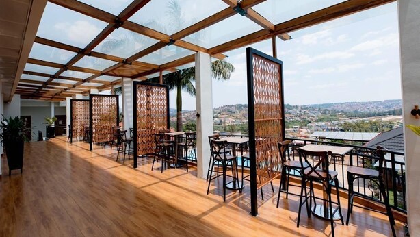 An open-plan restaurant with wooden flooring and high ceilings, featuring multiple tables and chairs, and a view of a cityscape. - Kigali Delight Hotel (Kigali)