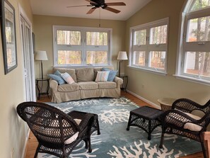 A living room with a beige sofa, two wicker chairs, a patterned rug, and large windows with a view of trees. - Ohana Sunrise - VERY NICE 3BR, Close to the beach - Linens & Towels provided (Chincoteague)
