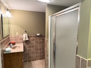 A bathroom with a sink, mirror, towel ring, and a shower stall.