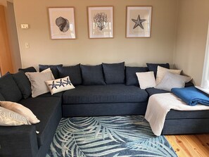 A dark-colored sofa with multiple cushions, a patterned rug, and three framed marine-themed artworks on the wall. - Ohana Sunrise - VERY NICE 3BR, Close to the beach - Linens & Towels provided (Chincoteague)