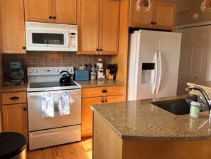 A kitchen with wooden cabinets, a white microwave, a stove, a refrigerator, and a coffee maker.