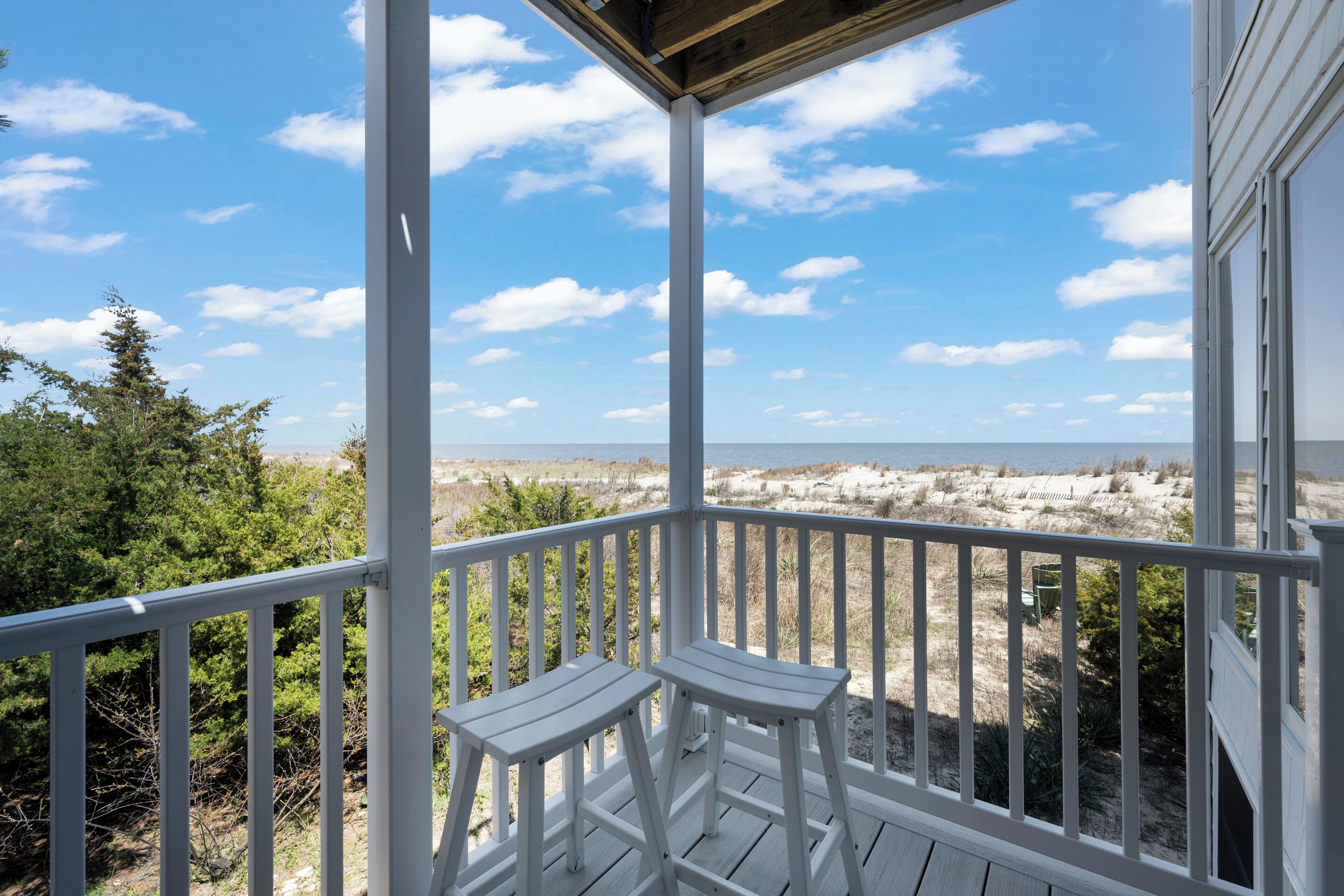 A wooden deck with white railings overlooking a beach.