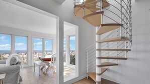 Una habitación amplia con una escalera espiral, ventanas grandes y vistas a la playa.