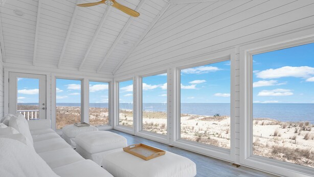 Una habitación amplia con vigas de madera blanca, ventanas grandes y vista a la playa.