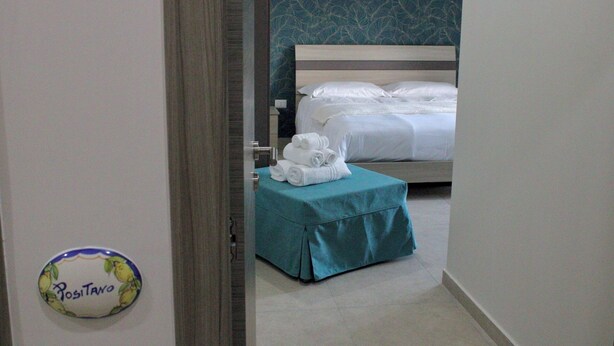 Une chambre d’hôtel avec un lit, une table de chevet de couleur turquoise sur laquelle sont posées des serviettes, et un panneau fixé au mur.