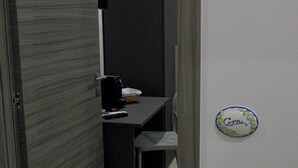 Une pièce avec une porte en bois sombre, une petite table sur laquelle se trouvent un panier et une télécommande, et une assiette décorative fixée au mur, portant le mot « Capri ».