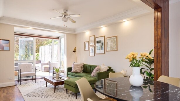 A modern living room with a green sofa, a round glass table, and a ceiling fan. - The Randall Retreat Spacious 4bdr Home With Garden (London)