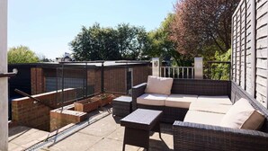 A rooftop patio with wicker furniture, a small table, and a brick planter. - The Randall Retreat Spacious 4bdr Home With Garden (London)