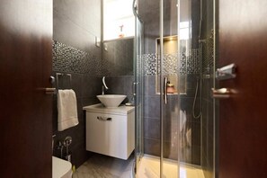 A modern bathroom with a glass-enclosed shower, a white sink, and a dark tiled backsplash. - The Radnor Mews Residence Stylish 3bdr Mews House (London)