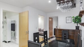 A modern dining area with a glass table and black chairs, a wooden door, and a kitchen area with a plant and a framed picture. - Cozy 2 Bedrooms, Devons Road DLR (London)