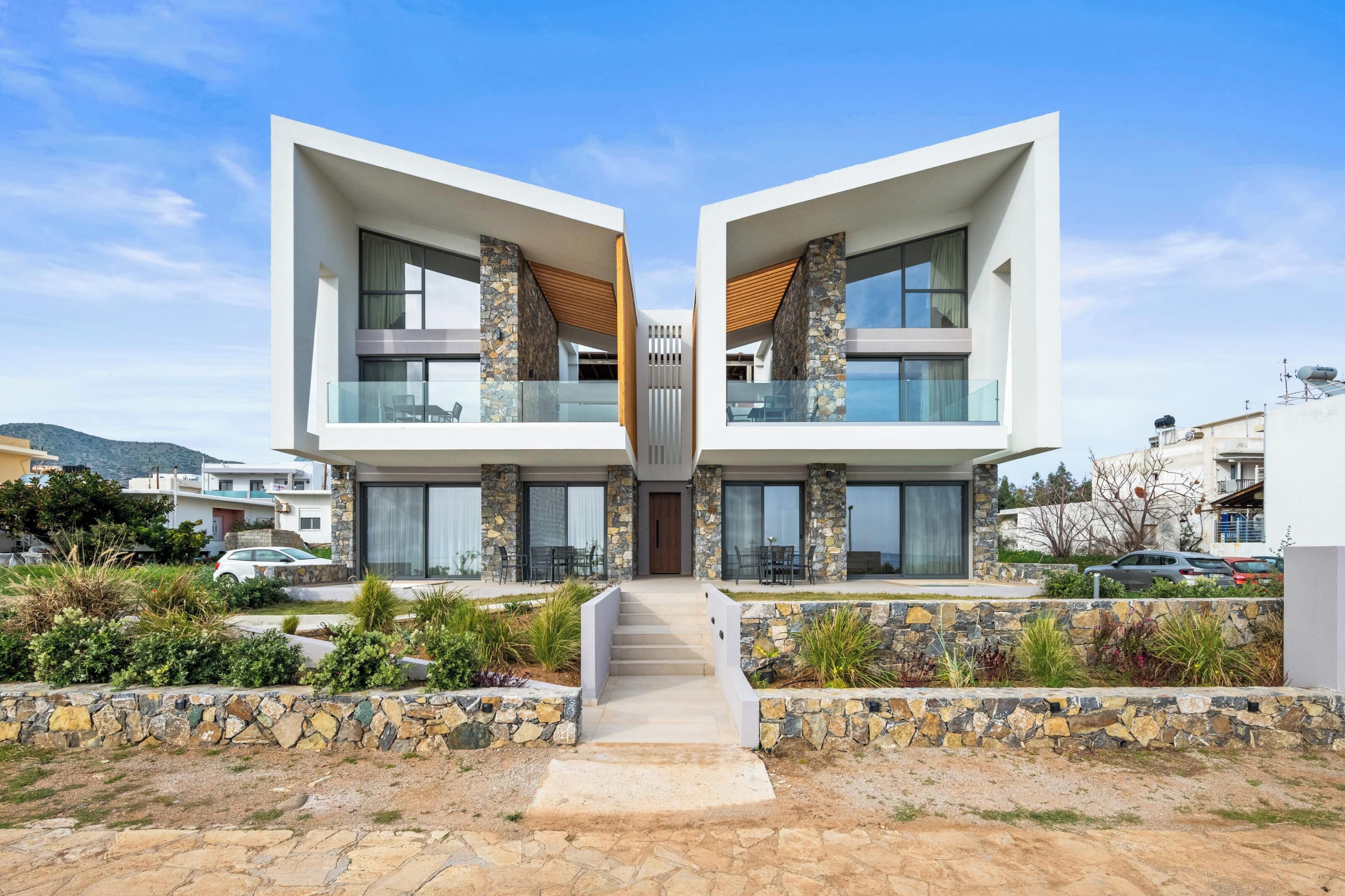 A modern two-story house with a symmetrical design, featuring a central staircase, stone pillars, and large windows.