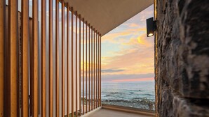 Ein Balkon mit Meerblick bei Sonnenuntergang, aus Holzlamellen und einer Steinmauer.