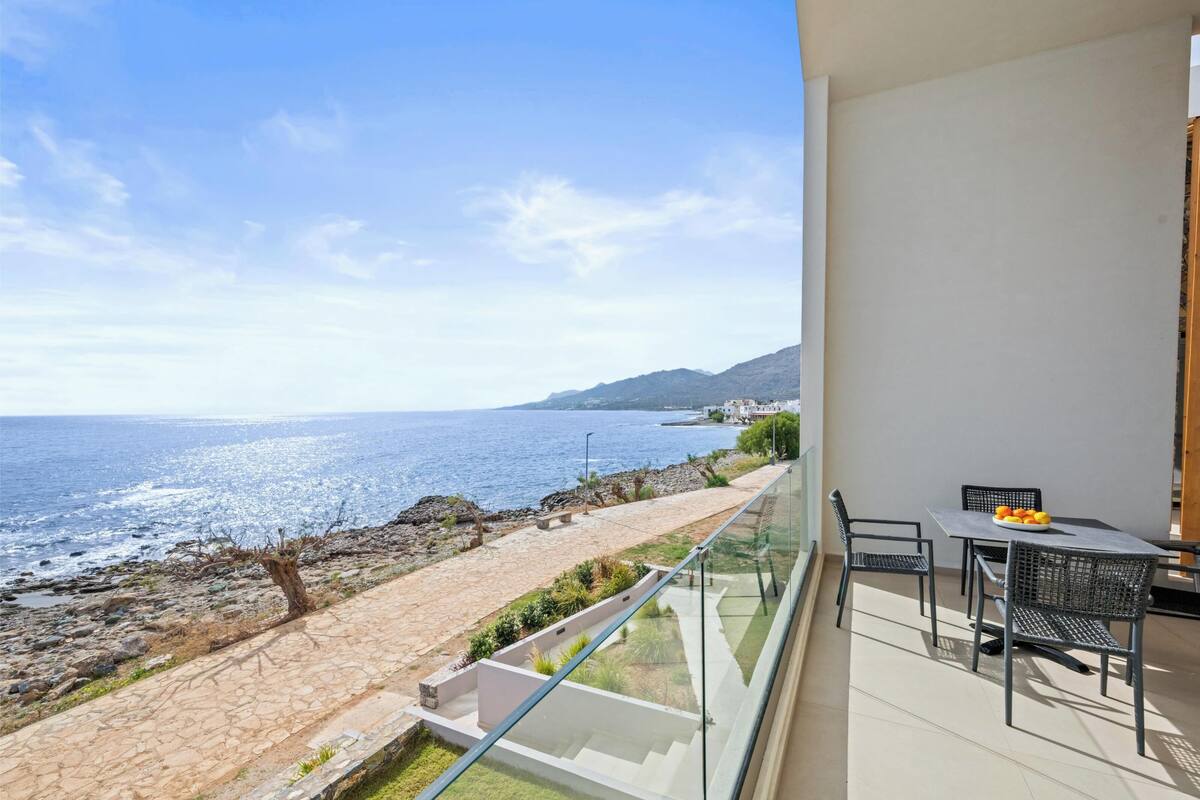 A balcony with a glass railing overlooking a rocky shoreline and the sea.