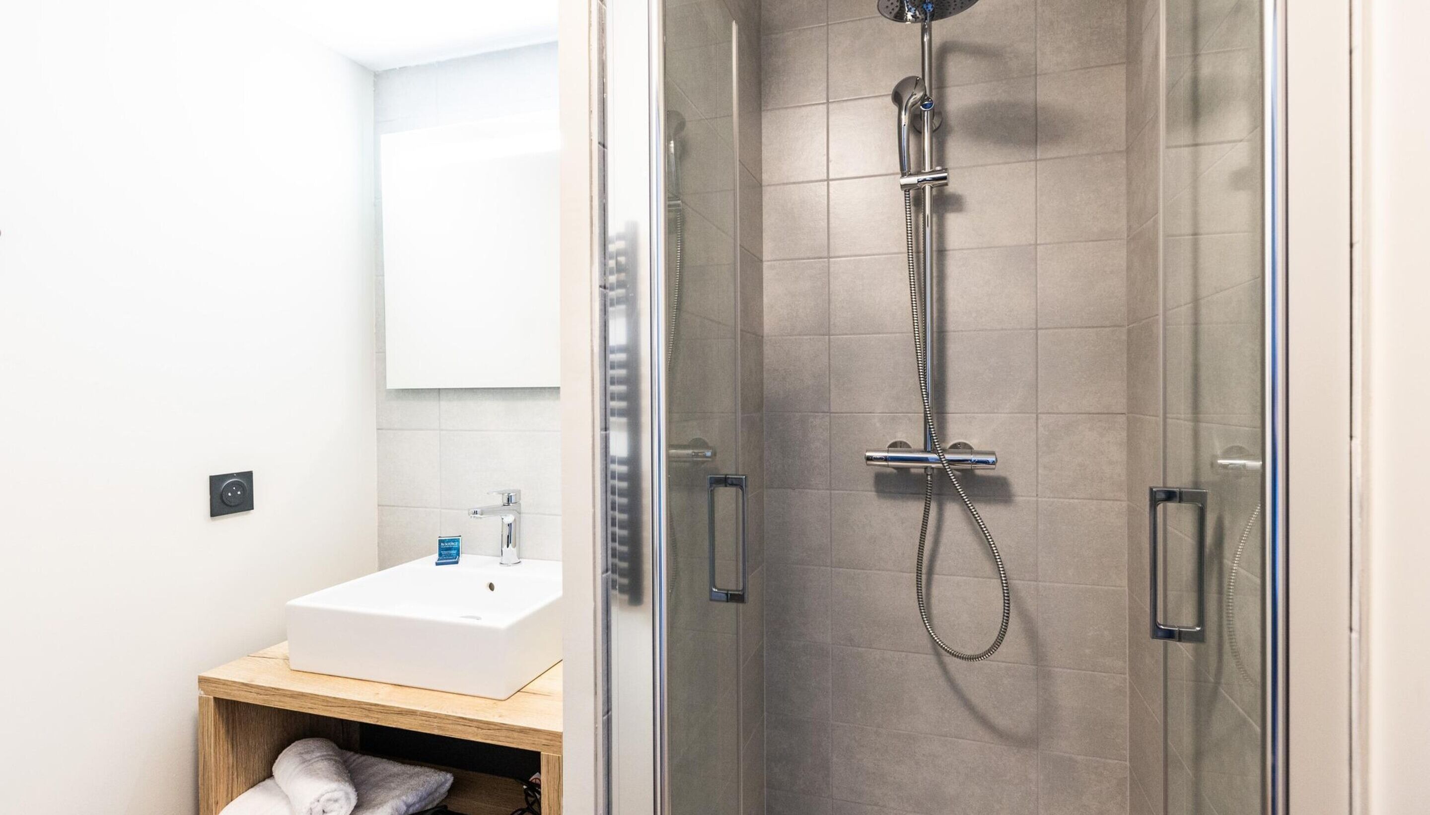 Een moderne badkamer met een douchecabine van glas, een witte wastafel en een houten wastafelmeubel.