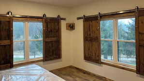 A bedroom with wooden sliding doors, a bed, and a window with a view of trees.