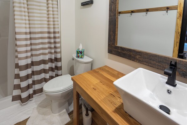 A bathroom with a wooden vanity, a white sink, a toilet, and a striped shower curtain.