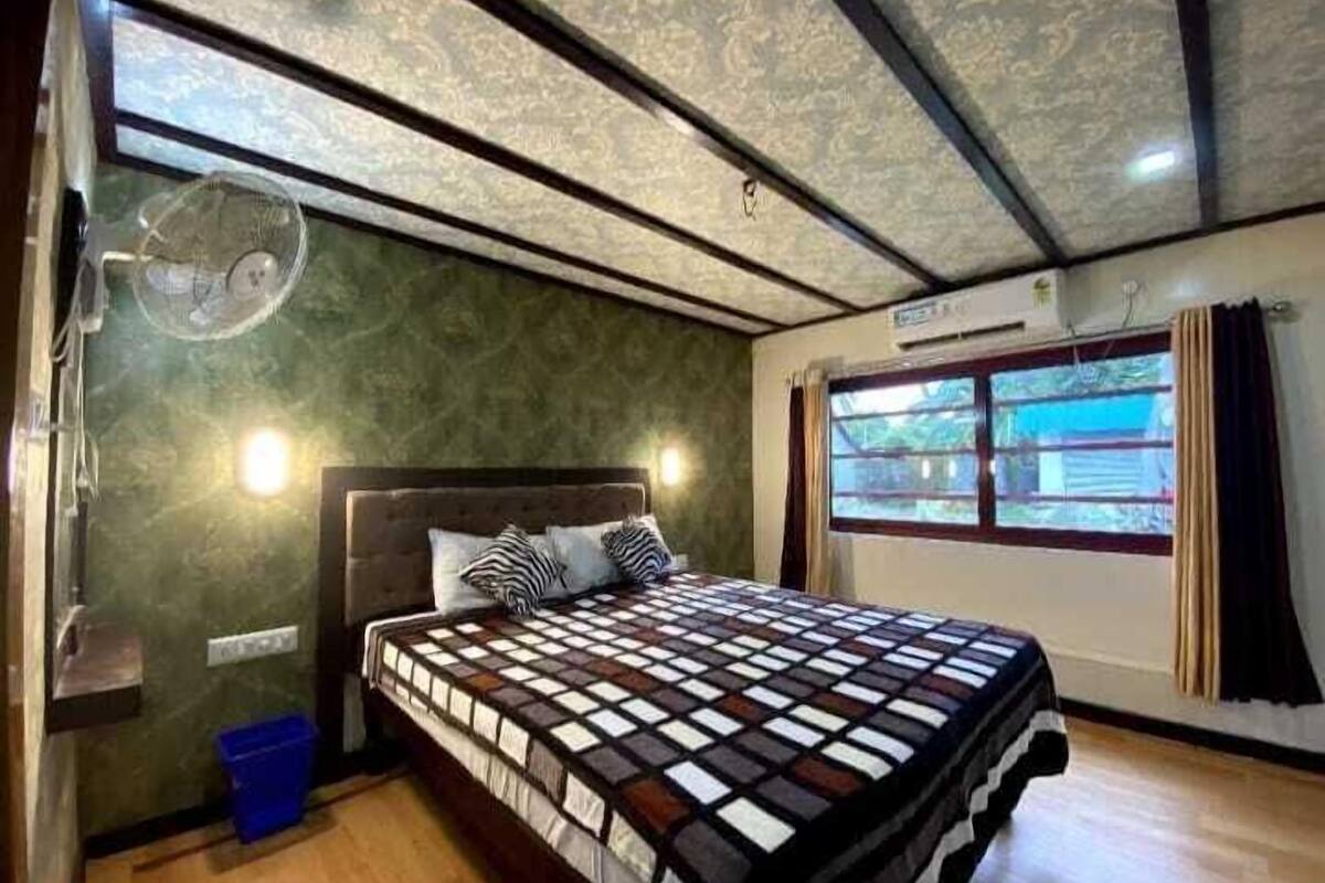 A bedroom with a bed, a fan, a window, and a wall-mounted air conditioner.