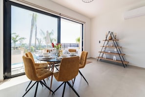 A dining area with a table set for four, large windows, and a decorative shelf.