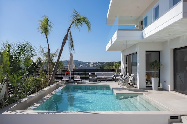 A modern pool area with lounge chairs, a palm tree, and a view of the city.