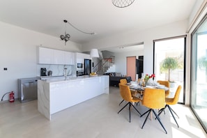 A modern kitchen with white cabinets, a central island, and a dining area with yellow chairs.