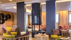 A cozy lounge area with a central wood-burning stove, comfortable seating, and a wooden wall. - Apartment in Alps With Spa & Pool (Tignes)