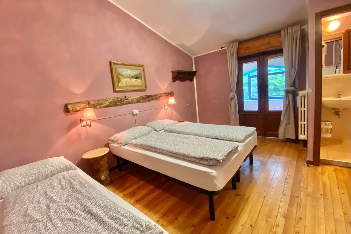 A bedroom with two beds, a wooden floor, a window with curtains, and a painting on the wall.