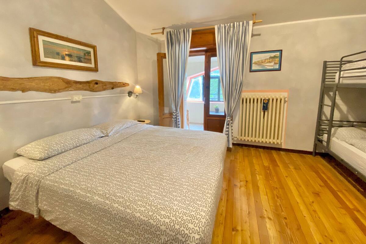 A bedroom with a bed, a bunk bed, wooden flooring, a radiator, and a window with curtains.