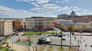 Una plaça urbana amb un edifici gran amb cúpula al fons, envoltada d'altres edificis i un cel serè.
