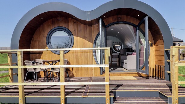 A modern, curved structure with a wooden interior and a small outdoor seating area. - The Hazel Hobbit Pod (Cowbridge)