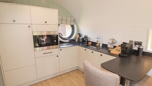 A compact kitchen with white cabinets, a built-in oven, a microwave, a sink, and a coffee maker. - The Hazel Hobbit Pod (Cowbridge)